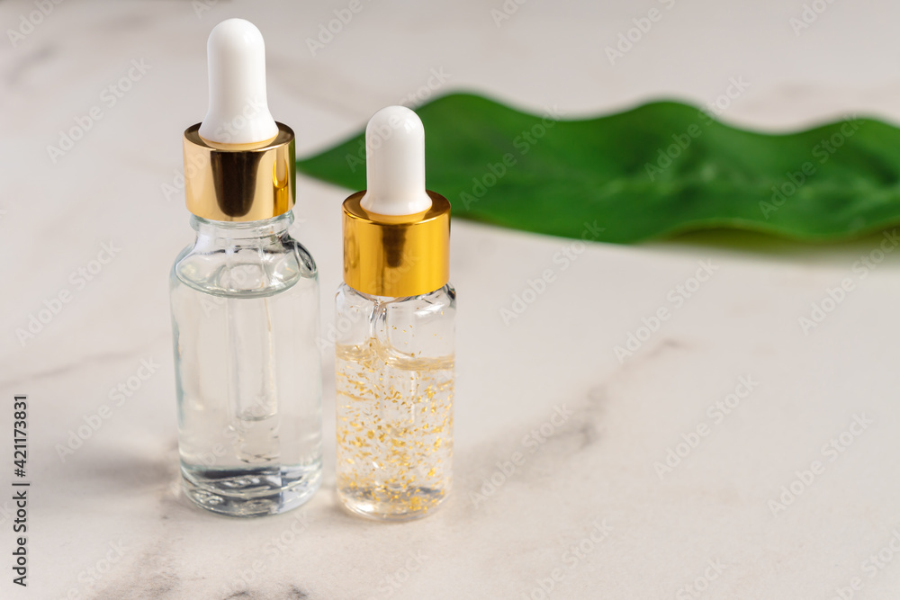 set of a glass cosmetic bottles with a dropper on a marble background with leaves. Natural cosmetics concept, natural essential oil with 24K gold inclusions set of a glass cosmetic bottles with a dropper on a marble background with leaves. Natural cosmetics concept, natural essential oil with 24K gold inclusions