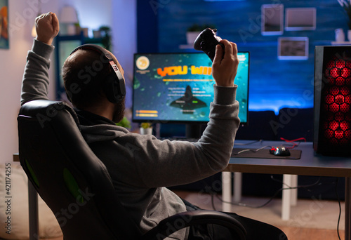 Winner gamer sitting on gaming chair at desk and playing space shooter video games with controller. Man streaming online videogames for esport tournament in room with neon lights photo