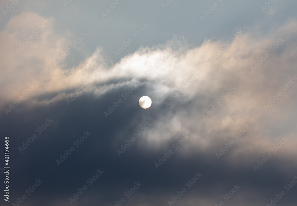 The sun shines behind the clouds during