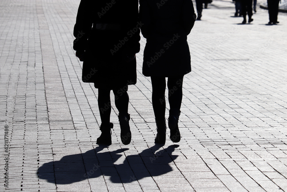 Silhouettes and shadows of two women walking down the street on people background. Concept of female friendship, demography, city life