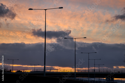 Spectacular red sunset with dark rainy clouds over the bridge with silhouettes of people and vehicles and tall street lanterns along highway M50 in Dublin, Ireland. Beautiful cold sunset clouds