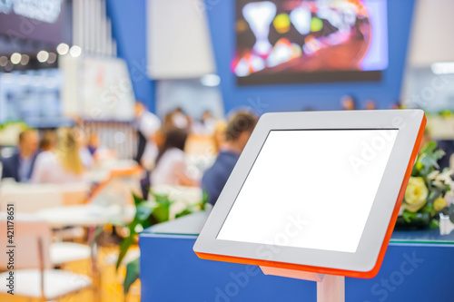 Electronic multimedia tablet kiosk with blank white display at exhibition, trade show, conference - close up view. Mock up, futuristic, corporate, copyspace, template, white screen, technology concept