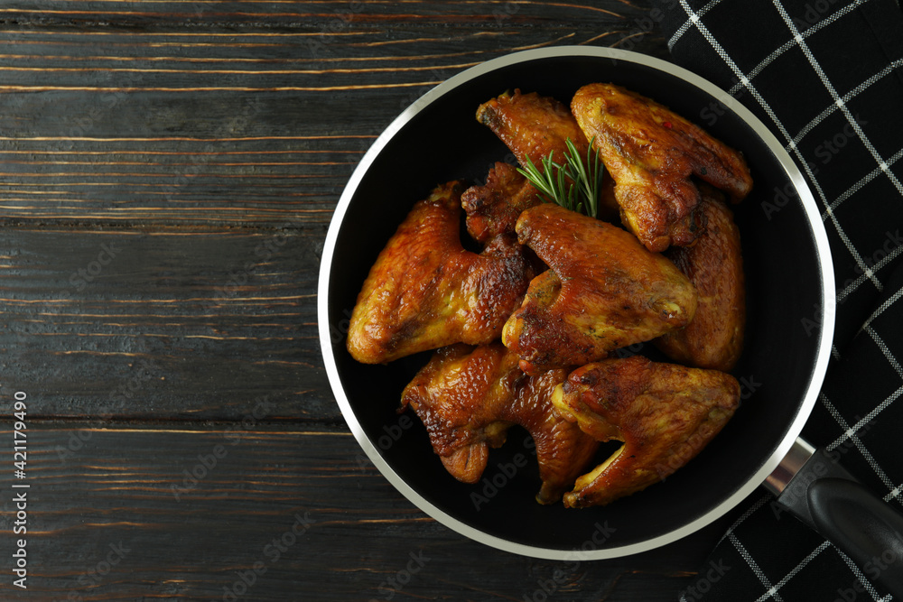 Pan with baked chicken wings and kitchen towel on wooden background Pan with baked chicken wings and kitchen towel on wooden background