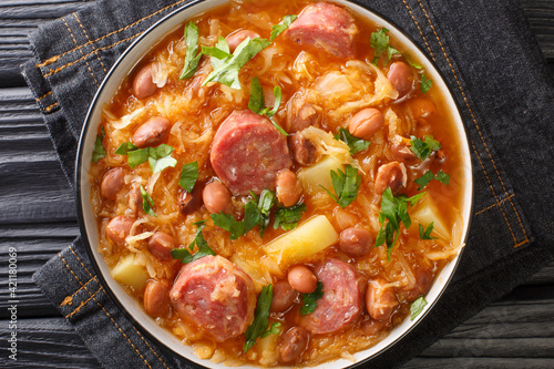 Thick sauerkraut soup with borlotti beans, potatoes and sausages close-up in a bowl on the table. horizontal top view from above