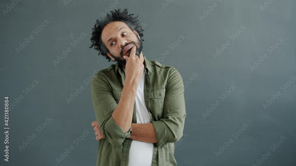 Slow motion portrait of middle-aged Arab man thinking touching beard standing on gray background concentrated on ideas. People and emotions concept. Slow motion portrait of middle-aged Arab man thinking touching beard standing on gray background concentrated on ideas. People and emotions concept.