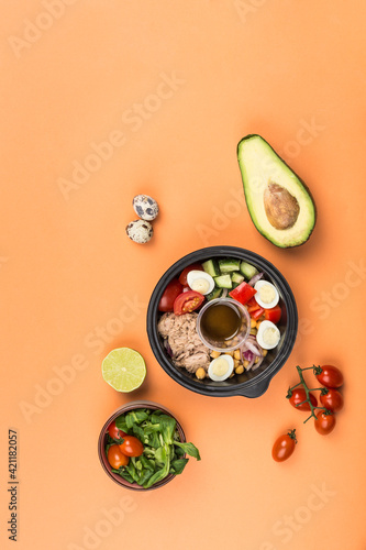 Vegetable bowl with tuna, fresh tomatoes, cucumber, quail egg, corn, red onion and sauce on an orange background.