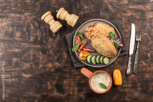 Kiev-style cutlets on a flat plate with fresh vegetables on a wooden background with sauce and eating utensils.