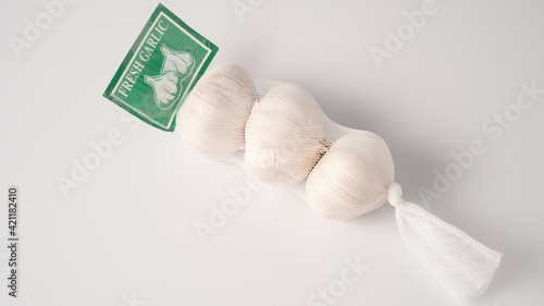 Garlic in net. Garlic packaging nets. Three garlic heads packaged in a mesh bag. Fresh garlic head wrapped in mesh bag