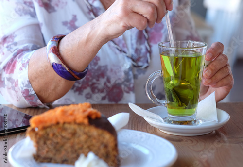 Close-up on woman's hand in coffee shop, enjoying an herbal tea and a slice of carrot cake