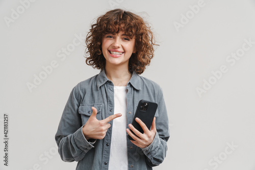 Young excited woman holding and pointing finger at mobile phone