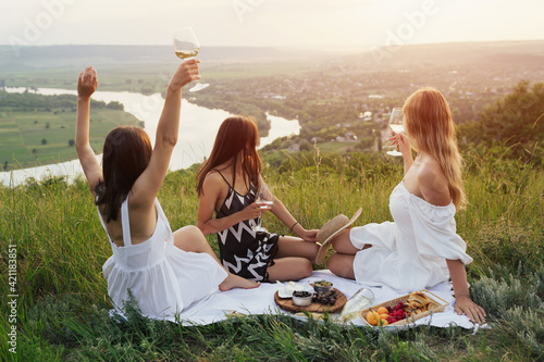 Young happy girls enjoying picnic time and beautiful landscape from the hill in summer sunny day.