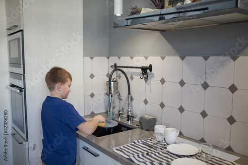 Side view portrait of smiling boy washing dishes at home while standing by sink in kitchen  copy space