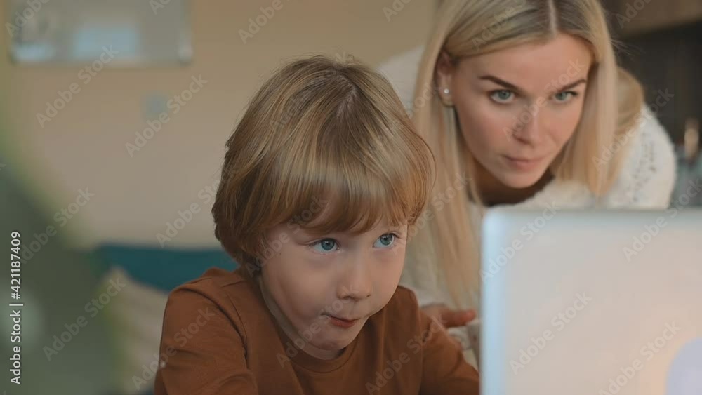 Little boy having online class with laptop at home, mother helping Little boy having online class with laptop at home, mother helping