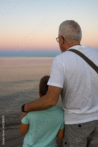 Grandfather and his grandson looking the ocean at sunset