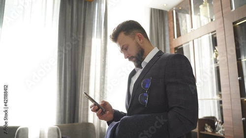 Thoughtful businessman with mobile phone stand in contemplation, thinking about something, in elegant suit.