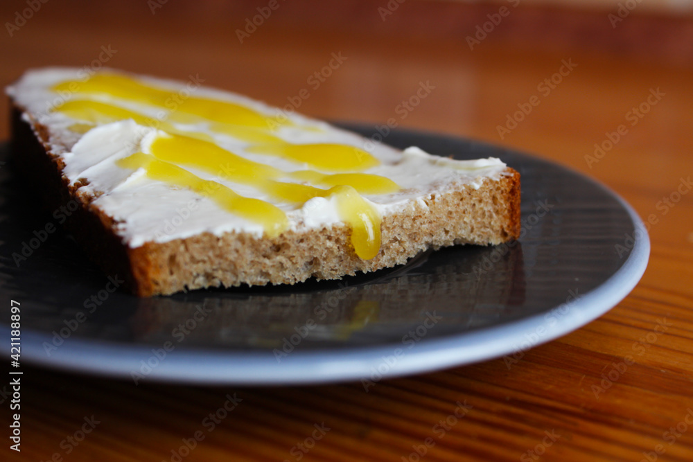 A slice of bread, spread with cheese and butter, sprinkled with yellow syrup with honey on a plate. Well-fed breakfast. Selective focus and blurred background. A slice of bread, spread with cheese and butter, sprinkled with yellow syrup with honey on a plate. Well-fed breakfast. Selective focus and blurred background.