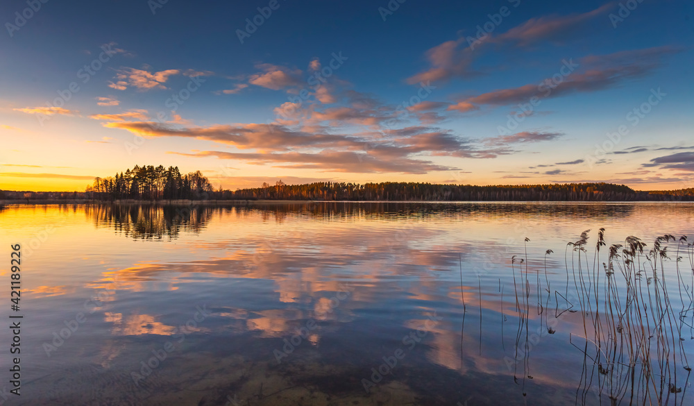 Epic red sunset sky above the lake and forest. Dramatic cloudscape. Symmetry reflections on the water, natural mirror