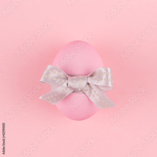 Elegant easter egg with silver bow on pastel pink background, square.