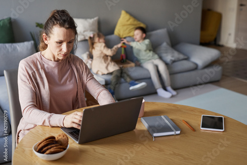 Canvas Print Portrait of single mother using laptop while working from home with two children