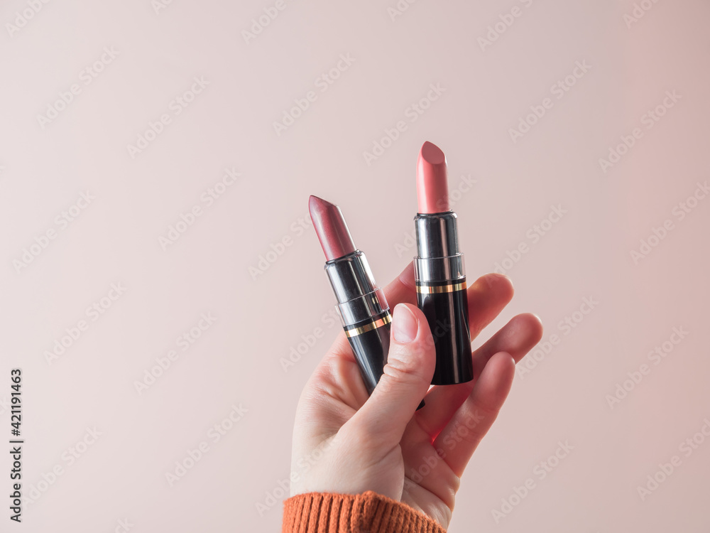 Obraz premium What lipstick should I use for my lips today? She holds open lipsticks in her hand. Powdery background