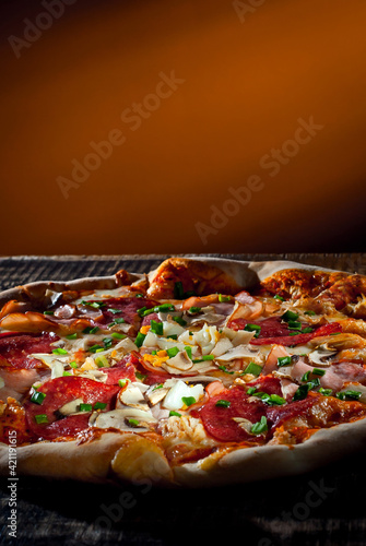 Round pizza on a wooden board. Pizza on orange background close up. Copy space and free space for text near food. contrasting dramatic light as an artistic effect.