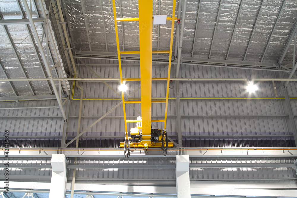Overhead crane inside factory or warehouse. That industrial machinery or lifting equipment consist of hoist, hook and wire rope traveling on beam girder structure. For manufacturing production plant. - obrazy, fototapety, plakaty 