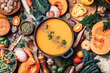 Pumpkin soup with vegetarian cooking ingredients, wooden spoons, kitchen utensils on wooden background. Top view. Vegan diet. Autumn harvest. Healthy, clean food and eating concept. Zero waste