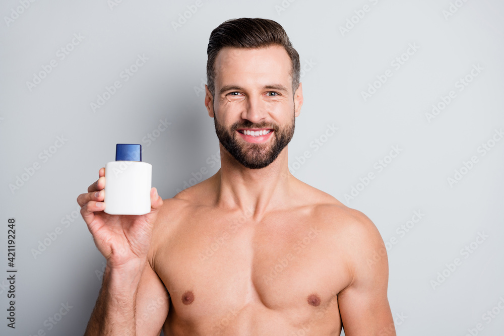 Close-up portrait of attractive cheerful well-groomed fit guy holding in hand bottle balm isolated over light grey color background Close-up portrait of attractive cheerful well-groomed fit guy holding in hand bottle balm isolated over light grey color background
