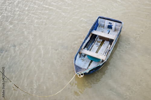 A small boat tied with a rope in the shallow water