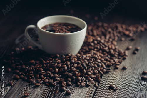 coffee beans scattered on a wooden table and a cup with a hot drink aroma