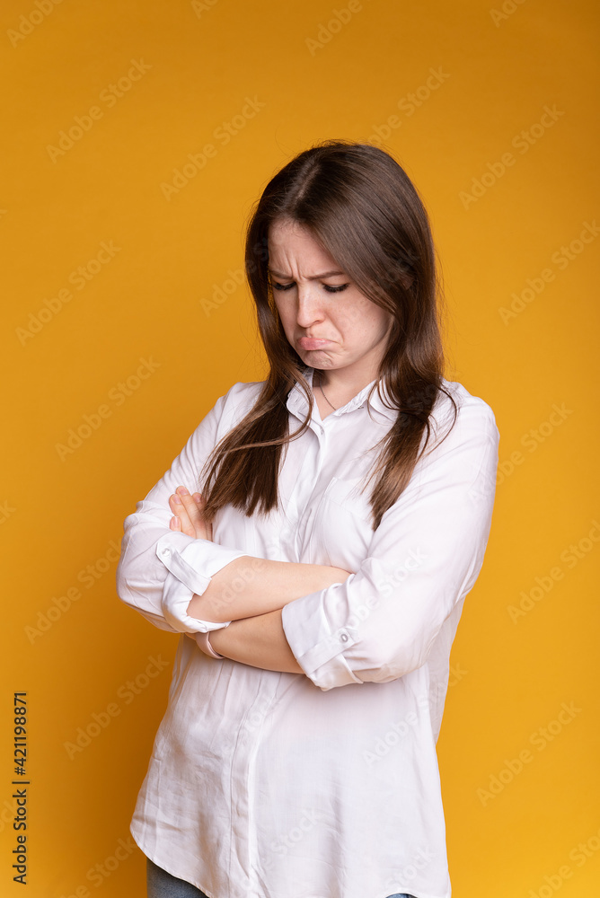 Portrait of frowning beautiful girl in white blouse, arms crossed on chest, on yellow isolated background Portrait of frowning beautiful girl in white blouse, arms crossed on chest, on yellow isolated background