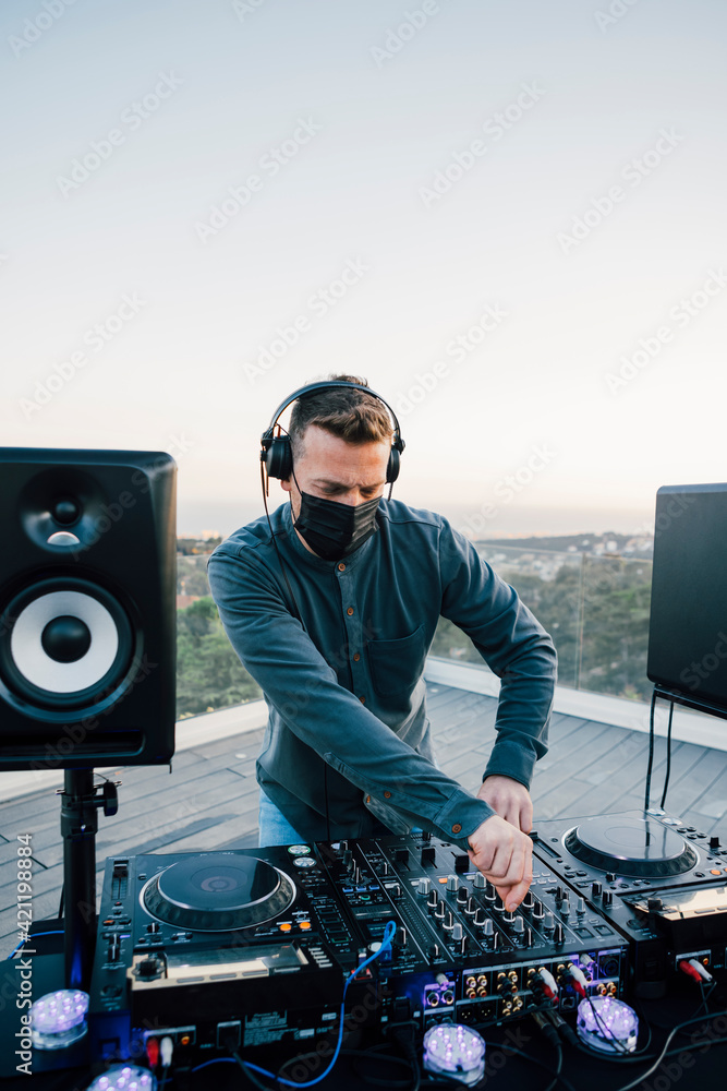 balance Monopol Shah Professional Disco DJ in face mask mixing songs with his mixer board,  playing music at a terrace house of a private party on summertime, with  mountain views, sunset. Copy-space. Stock-foto | Adobe