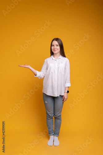Young woman on isolated yellow background holding imaginary copyspace on palm to insert ad