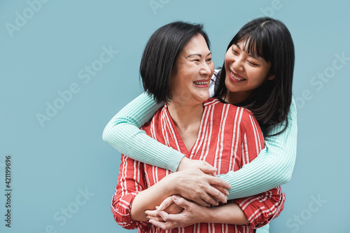 Fotografie, Obraz Asian mum and daughter hugging outdoors with blue wall in background - Mother da