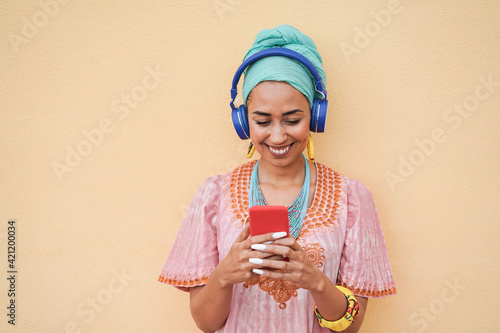 Fototapeta Young african woman listening music playlist while looking on mobile phone - Foc