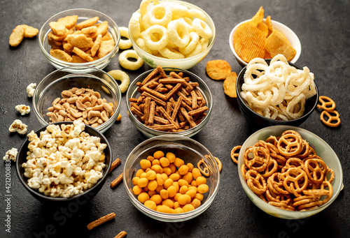 Assorted chips, popcorn, onion rings, croutons, cheese balls, biscuits in bowls. unhealthy food for figure, heart, skin, teeth. An assortment of fast carbohydrates. Junk food on a stone background
