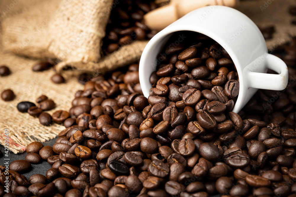 Coffee beans roasted in a white cup with were placed on a sackcloth on a black stone floor. Coffee beans roasted in a white cup with were placed on a sackcloth on a black stone floor.
