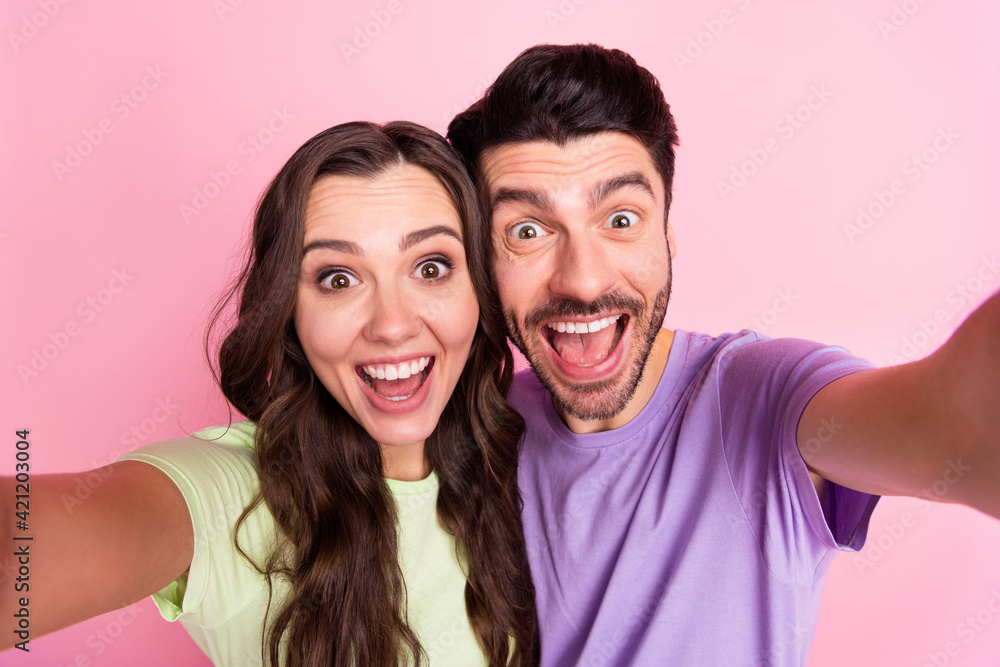 Self-portrait of attractive amazed cheerful couple embracing having fun good mood isolated over pink pastel color background Self-portrait of attractive amazed cheerful couple embracing having fun good mood isolated over pink pastel color background