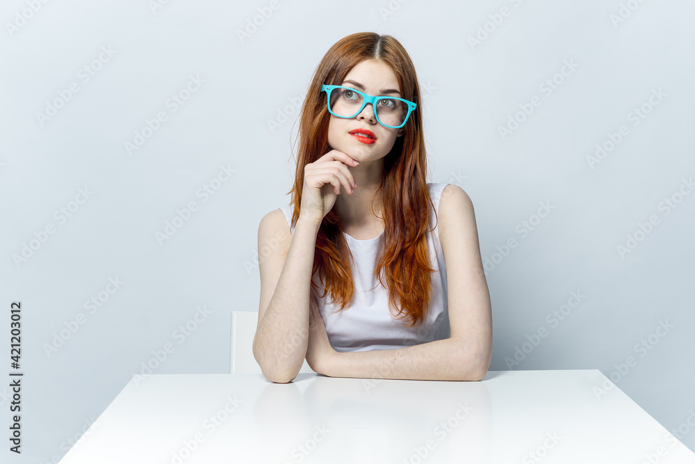 pretty red-haired woman sitting at the table wearing blue glasses red lips pretty red-haired woman sitting at the table wearing blue glasses red lips