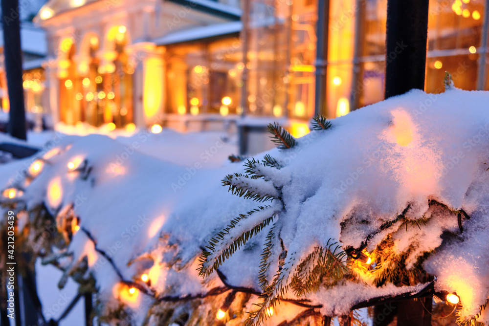 Snow-covered Christmas decorations with spruce branches and Christmas garlands on the street. Beautiful classic European architecture in the background.