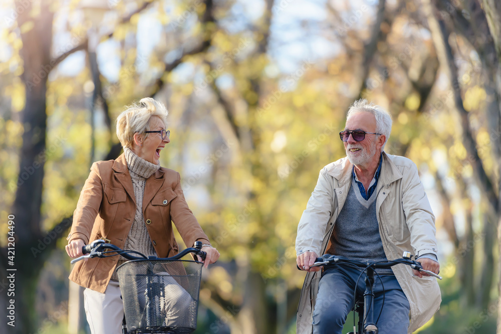 Obraz premium Cheerful active senior couple with bicycle in public park together having fun. Perfect activities for elderly people. Happy mature couple riding bicycles in park