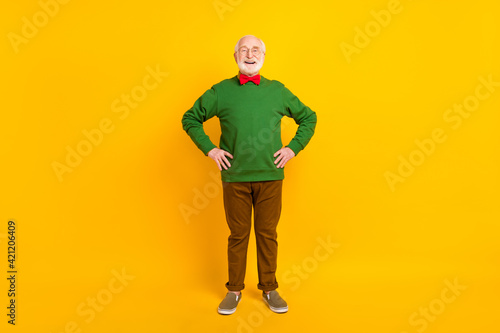 Full length photo of sweet confident mature man dressed pullover bow tie glasses arms waist smiling isolated yellow color background