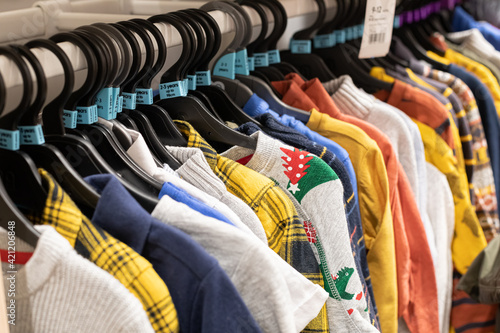 Retail store of children's clothing. Bright shirts, sweaters, sweatshirts hang on hangers. Nobody