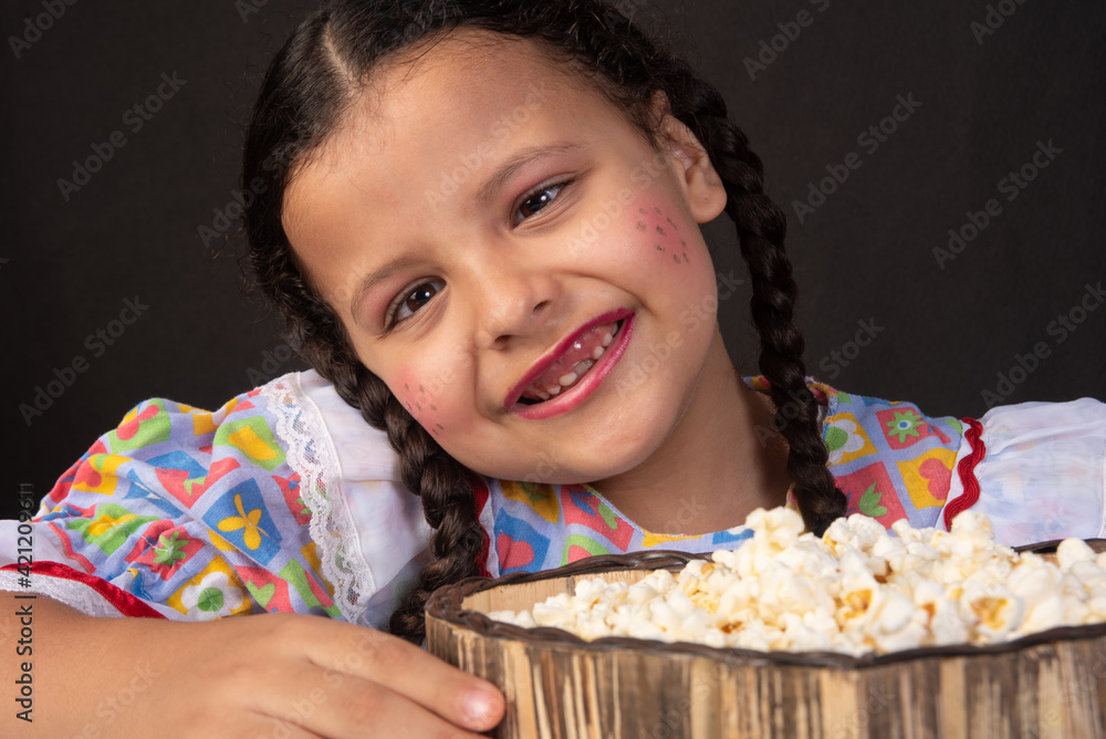 Festa junina in Brazil, brazilian girl with braids and dressed for junina party with popcorn, black background, selective focus. Festa junina in Brazil, brazilian girl with braids and dressed for junina party with popcorn, black background, selective focus.