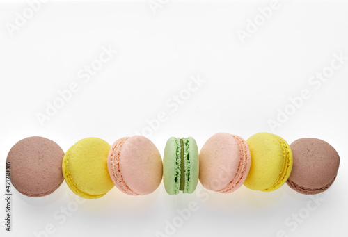 Horizontal photo of macaroon. Colorful cakes macaron with pastel tones laid out in a strip on white background. Free space on the top for your text. Top view of almond cookies.