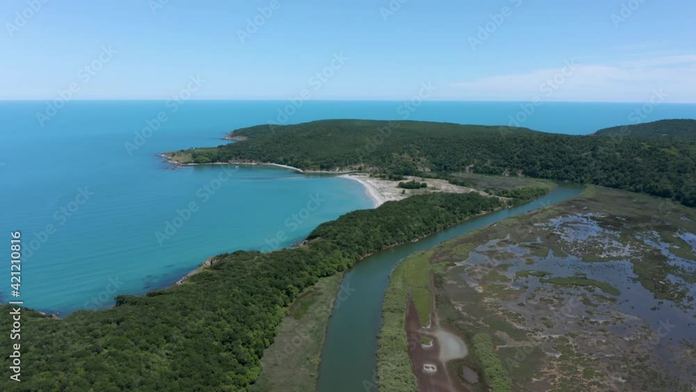 Drone flight above a river that passes by a dense green forest, a wild sandy beach and flows into the sea. Aerial view of the mouth of Ropotamo river in Ropotamo Natural Reserve, Bulgaria. Drone flight above a river that passes by a dense green forest, a wild sandy beach and flows into the sea. Aerial view of the mouth of Ropotamo river in Ropotamo Natural Reserve, Bulgaria.