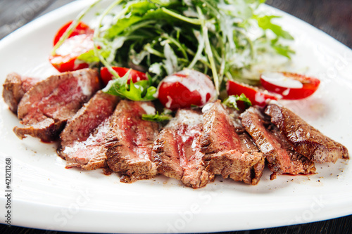 Closeup on sliced roast beef with greens and tomatoes on a white plate