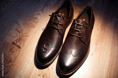 Leather stylish men s shoes with laces on a wooden floor with gold rings on a boot. Groom s wedding shoes. Classic shoes for men.