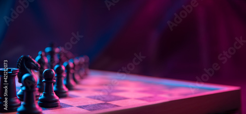 Print op canvas Chess pieces on a chessboard on a dark background shot in neon pink-blue colors