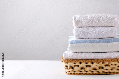 Clean fresh towels in the wicker basket on the white table against bright wall.Empty space